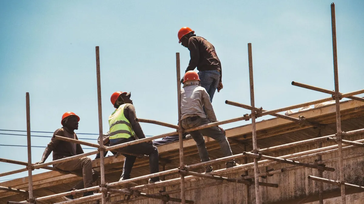 Construction workers in hard hats and reflective vests working on wooden scaffolding at a building site in Nairobi