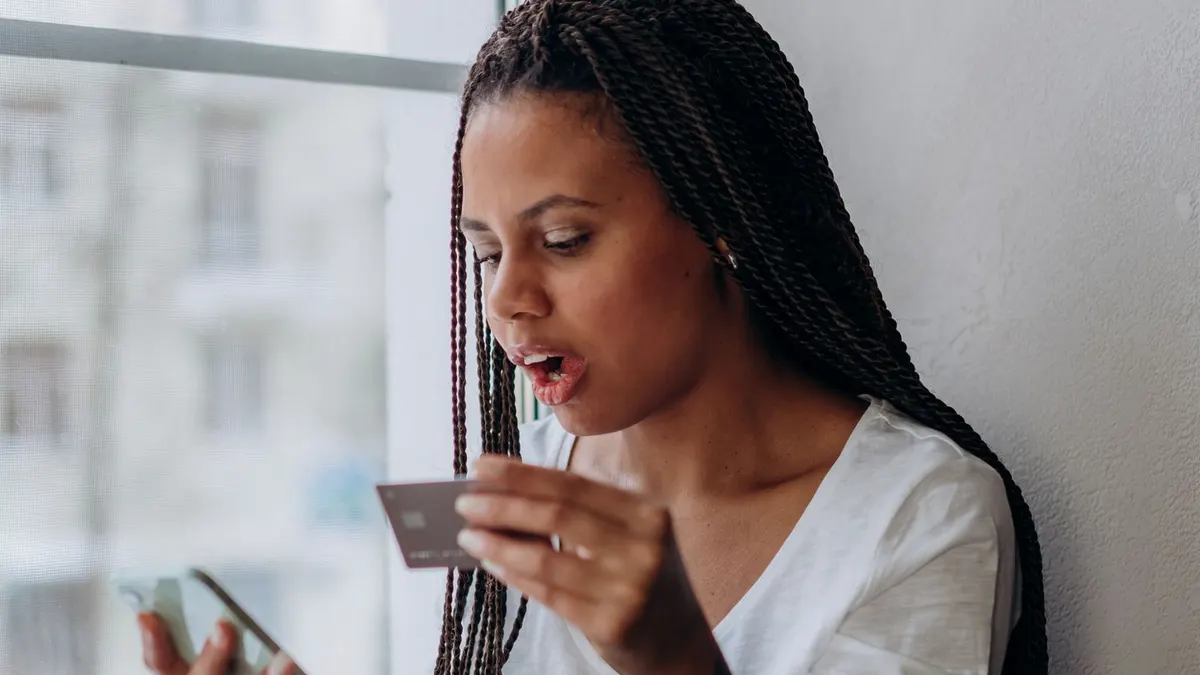 Young Black woman with braids checking her phone while holding a bank card