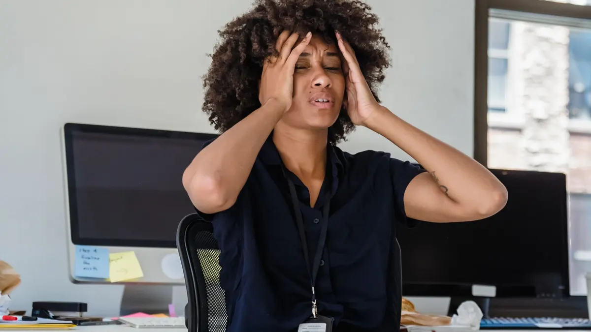 Frustrated young Black woman at an office desk with her hands on her head