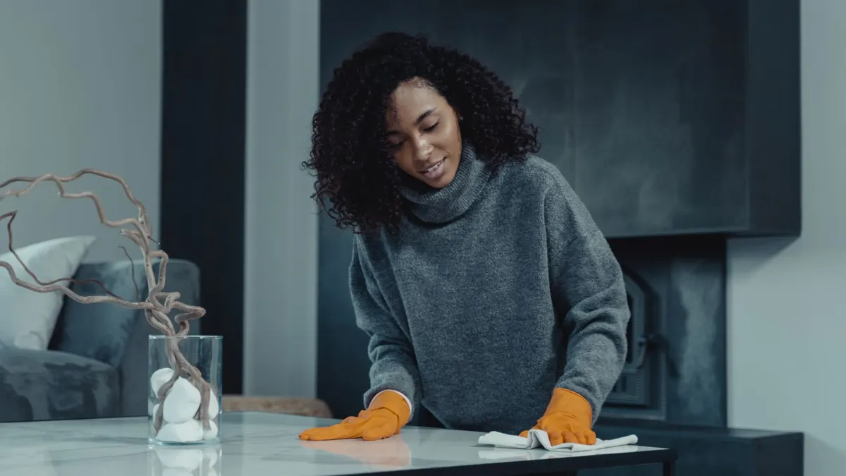 Woman in a grey sweater and gloves wiping a table in a home