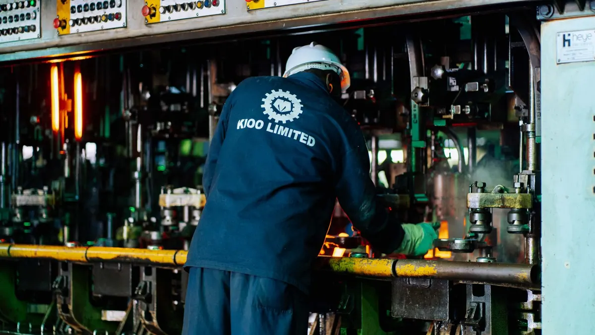 Factory worker in overalls operating glass manufacturing machinery