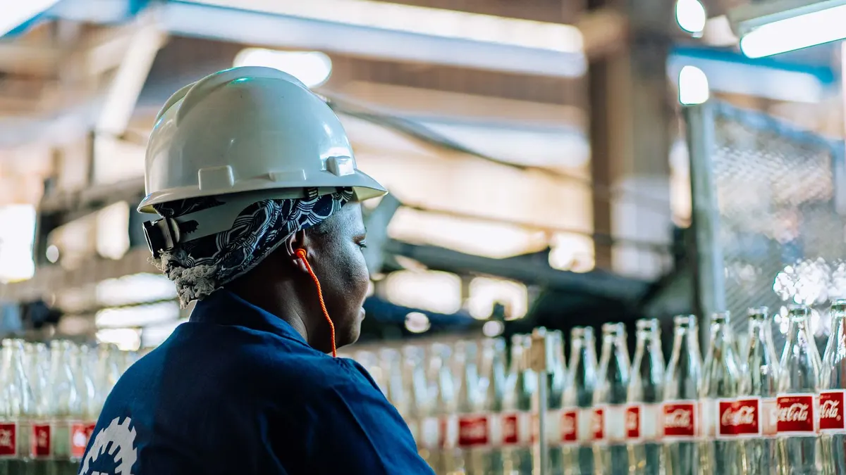 Factory worker in a hard hat checking glass bottles on a production line