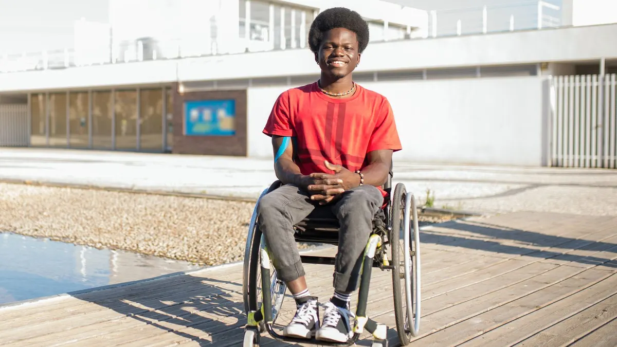 Smiling young Black man in a red T-shirt sitting in a wheelchair outdoors