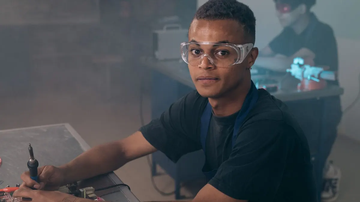 Young Black man in safety glasses working with a soldering iron in a workshop