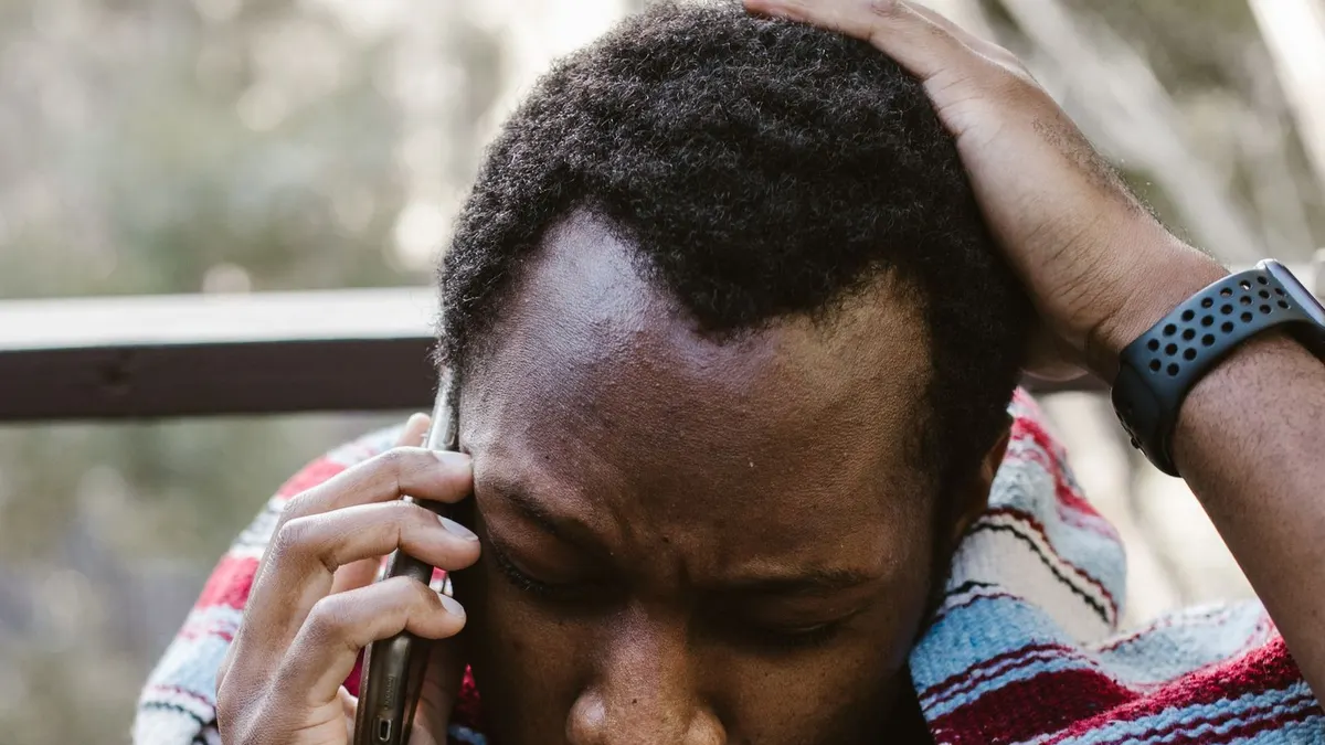 Worried young Black man holding his head while talking on a mobile phone