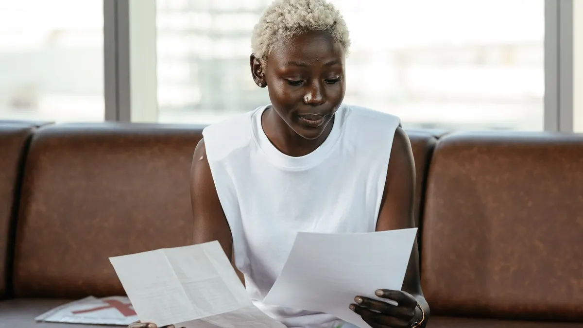 Woman with short bleached hair reading printed documents while seated on a brown office sofa