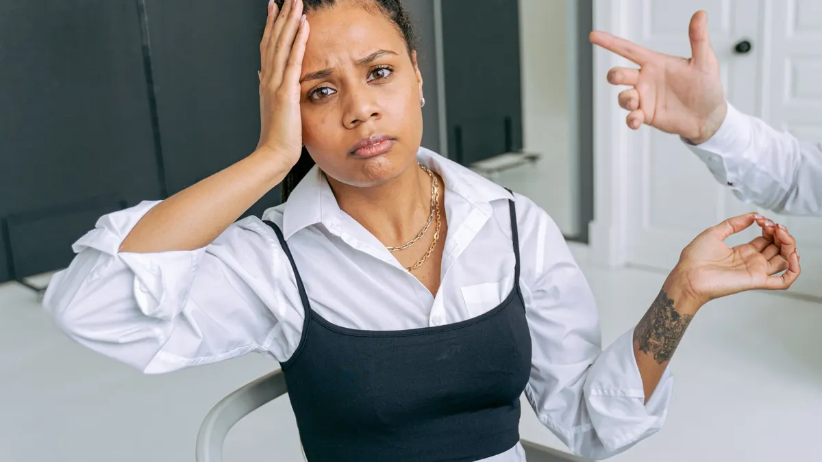 Woman sitting at an office desk looking uncomfortable as a colleague points at her