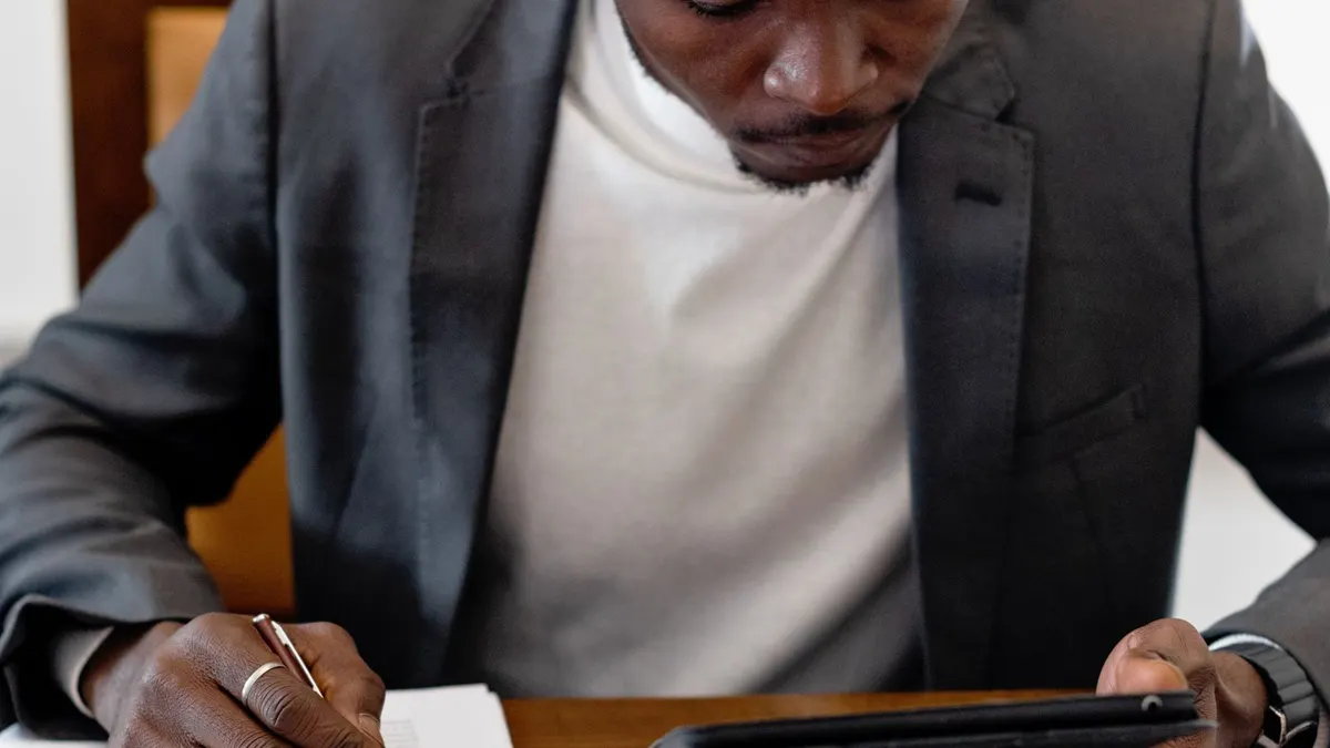 Young Black man in a suit at a desk reviewing documents with a tablet