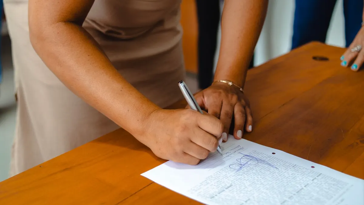 Close-up of a woman's hands signing a typed letter on a wooden office desk